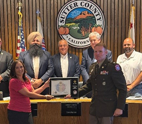 Veronica Baumgardner, HR Director for Sutter County, holding the ceremonial plaque with LTC Christopher Sadoski, NorCal BN CDR, with Sutter County Board Members in attendance
