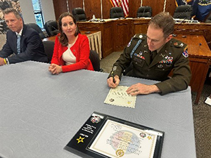 Mr. Joseph Butler, Mayor Sarah Pierce, look on while Col. Matthew Meyer signs the partnership Mr. Joseph Butler, Mayor Sarah Pierce, look on while Col. Matthew Meyer signs the partnership